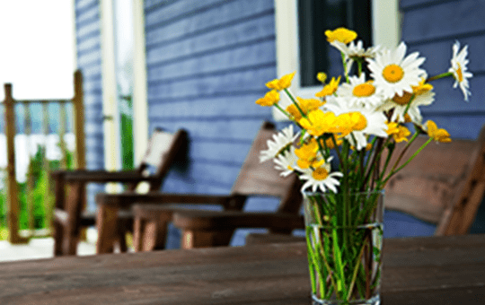 Cottage porch with patio chairs and daisies in a vase on the wooden table