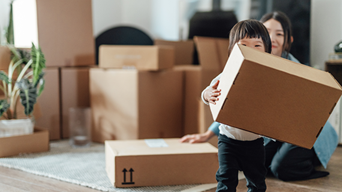 Moving day – young parent watching their daughter moving a cardboard box while being surrounded by other boxes